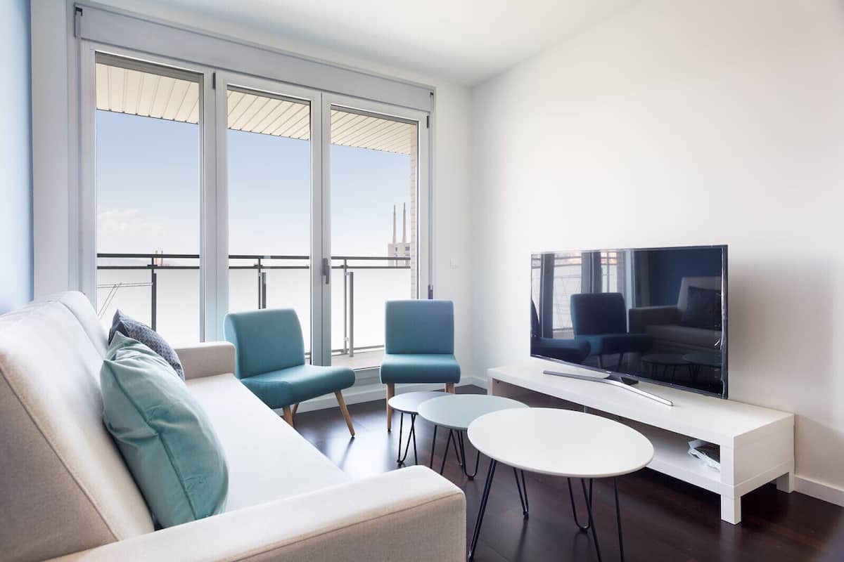 Un salon moderne avec un canapé, deux fauteuils, un téléviseur et un balcon doté d’une balustrade.