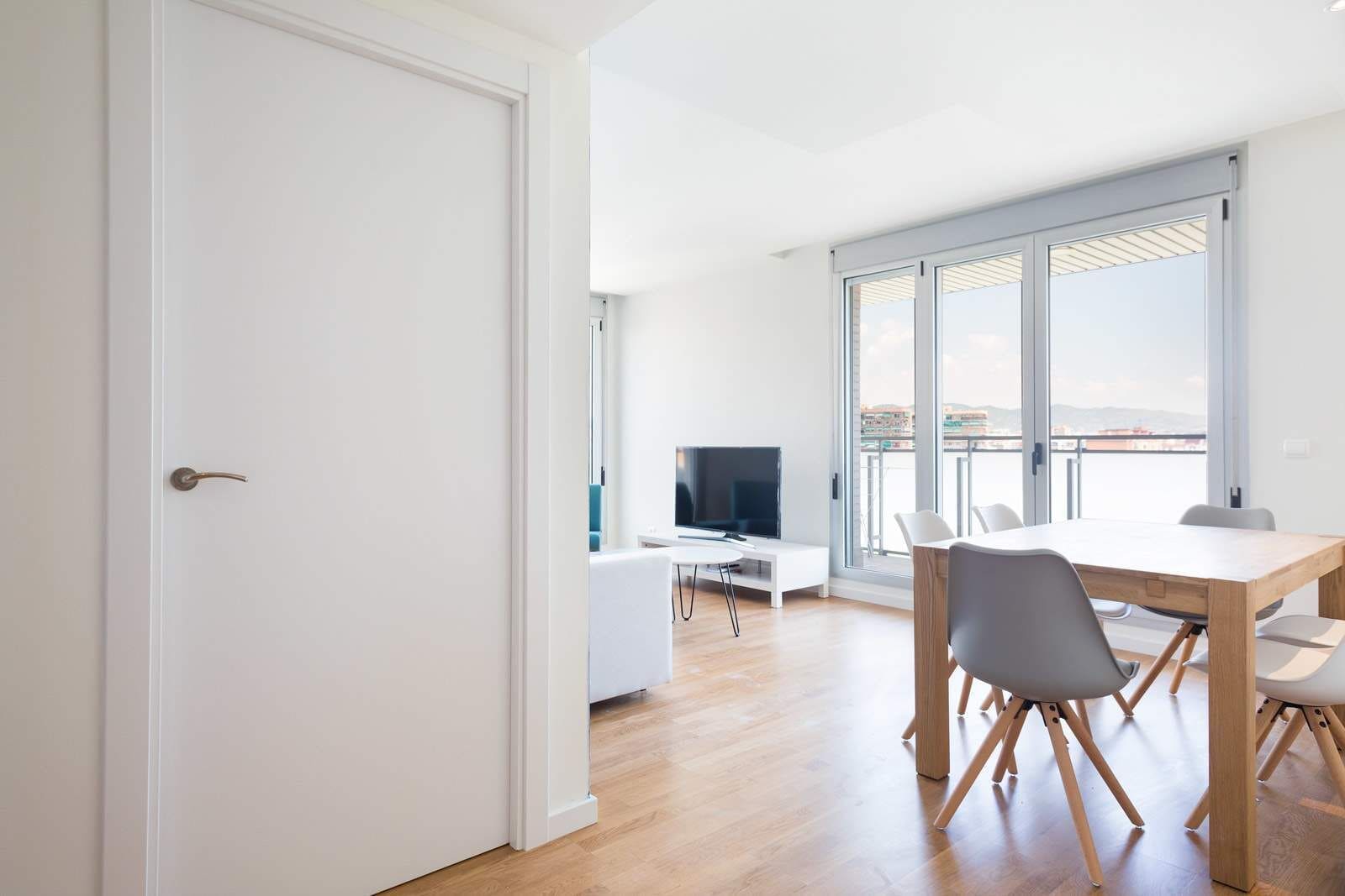 A modern apartment with a dining area, a TV, and large windows.