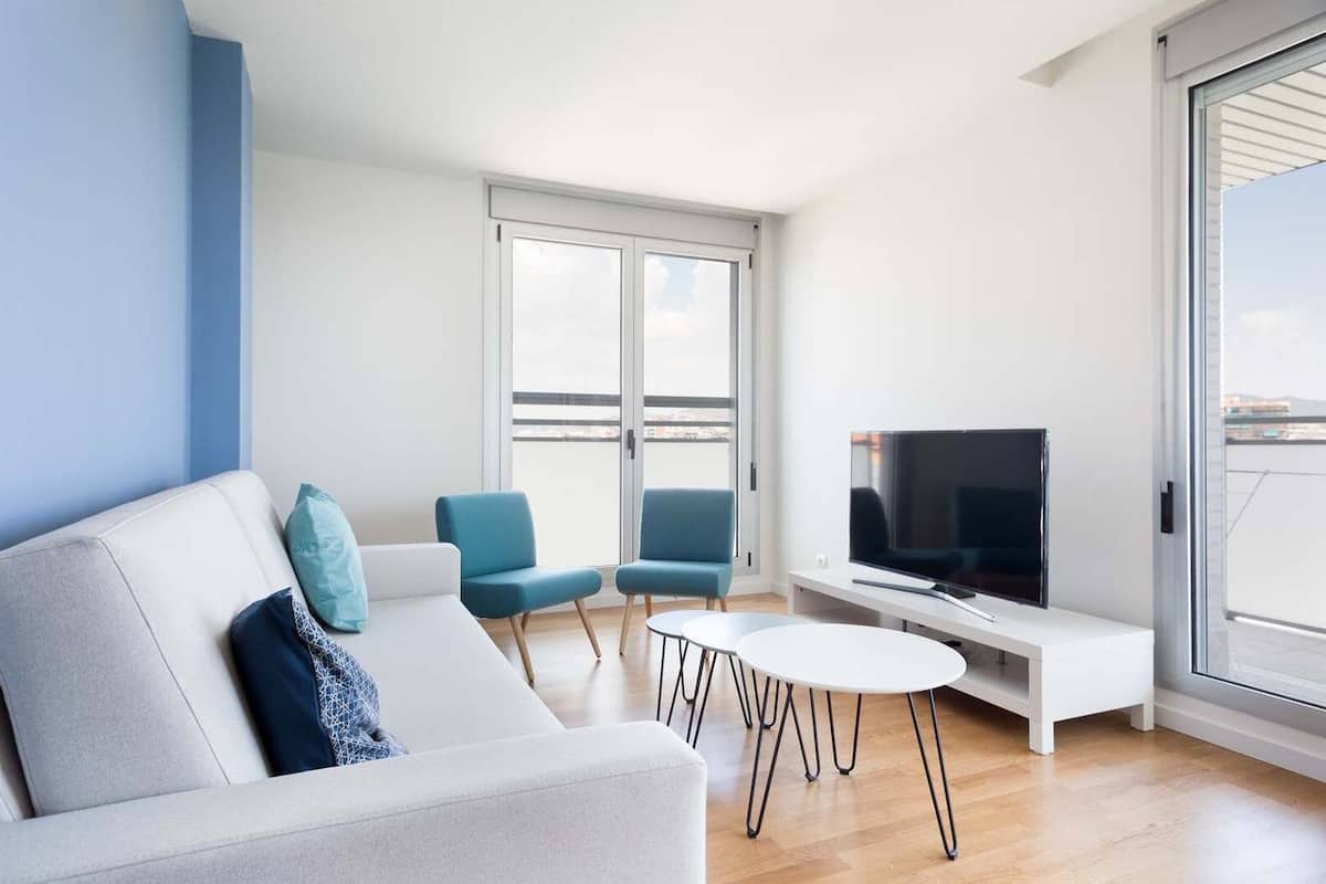 Un salon moderne avec un canapé, deux fauteuils, un téléviseur et un balcon.