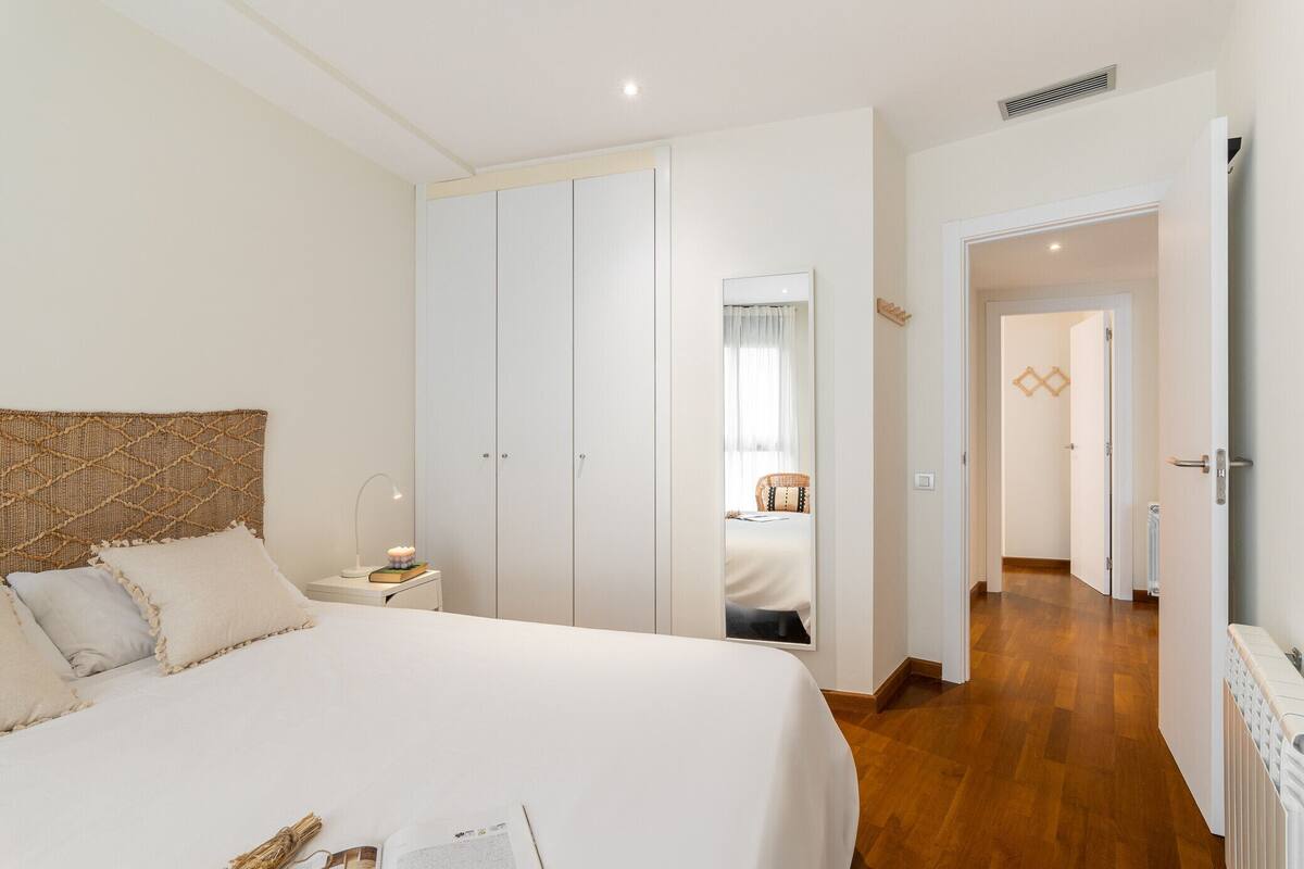 A bedroom with a large bed, a wardrobe, a bedside table with a lamp, and a mirror.