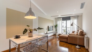 Una sala de estar moderna con un sofá, una mesa de comedor con sillas, una lámpara de pie y un ventanal con cortinas.