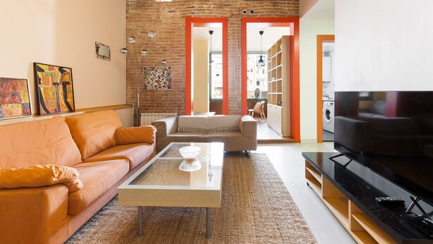 Un salon avec un canapé, une table basse en verre, un téléviseur et un mur en briques.