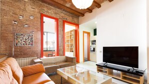 Un salon avec un mur en briques, des fenêtres à cadre orange, un canapé, une table basse et un téléviseur.