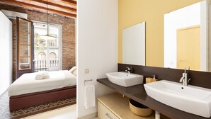 Une chambre avec un lit, une salle de bain avec deux lavabos, un miroir et une fenêtre.