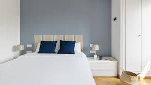 Un dormitorio con cama, dos lámparas de noche, una mesita de noche, una puerta y una cesta de mimbre.