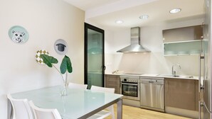 Una cocina moderna con electrodomésticos de acero inoxidable, una mesa de comedor de vidrio y sillas blancas.