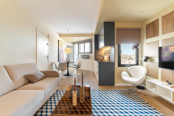 A modern living room with a sofa, a coffee table with candles, a patterned rug, and a city view through the window. - Sagrada Familia Apartment By Olala Homes (Barcelona)