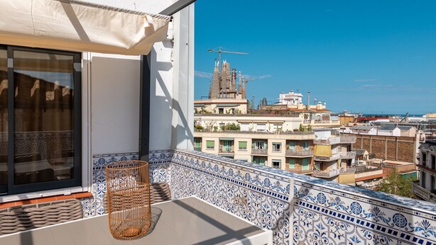 A balcony with a tiled floor, a wicker chair, and a view of a building with a distinctive architectural style.