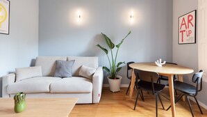 A modern living room with a sofa, a dining table, and chairs. There is a potted plant and a poster on the wall. - Señor Urgell Apartment By Olala Homes (Barcelona)
