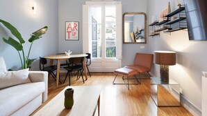 A modern living room with a sofa, a dining table with chairs, a coffee table, a lamp, a mirror, and a plant. - Señor Urgell Apartment By Olala Homes (Barcelona)