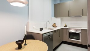 A modern kitchen with a dishwasher, oven, and a dining area with a table and chairs. - Señor Urgell Apartment By Olala Homes (Barcelona)