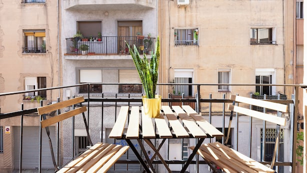 A balcony with a wooden table and chairs, a yellow pot with a plant, and a view of a multi-story building with balconies and windows. - Rafael Apartment by Olala Homes (L'Hospitalet de Llobregat)