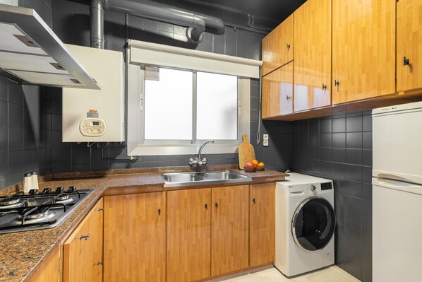 Una cocina moderna con armarios de madera, un lavamanos de acero inoxidable, lavadora incorporada y estufa a gas.
