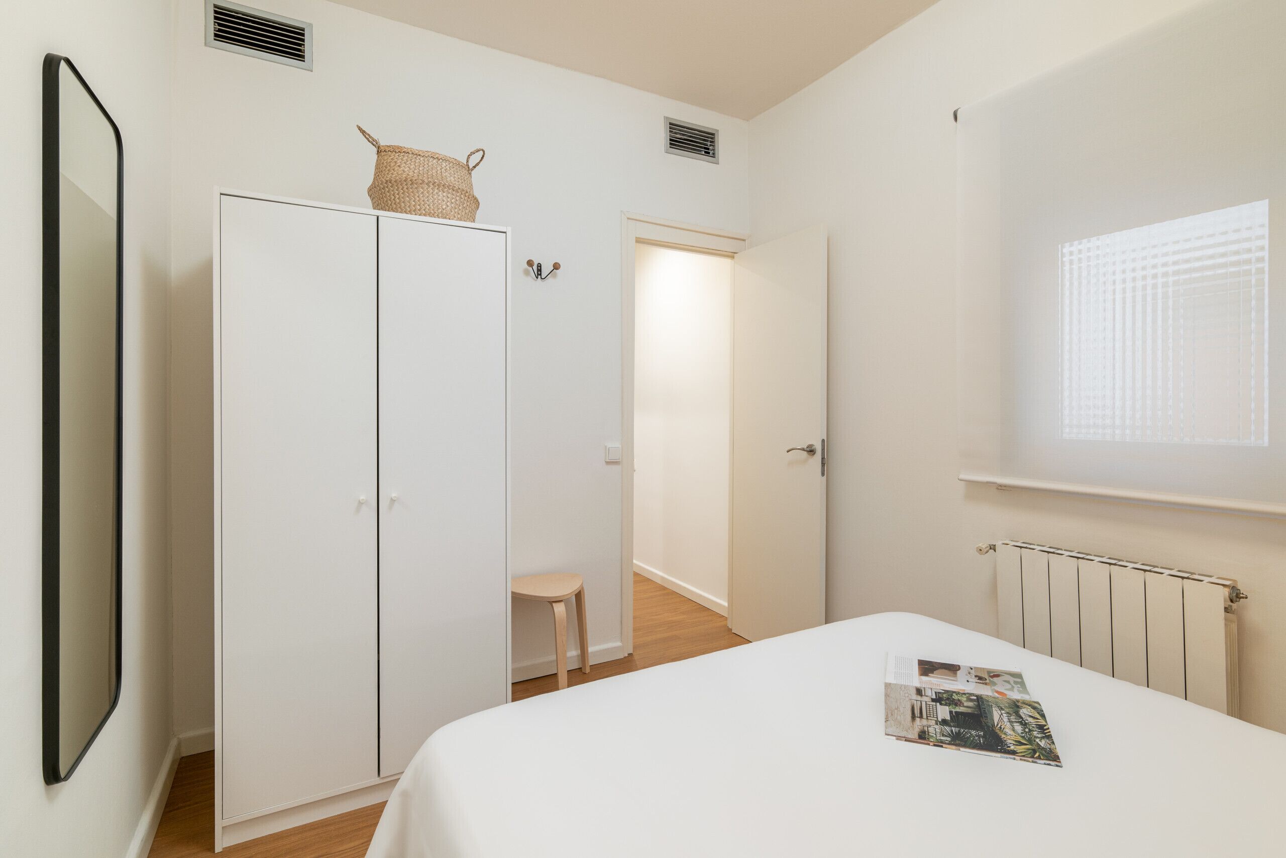 A bedroom with a bed, a wardrobe, a small stool, and a radiator.