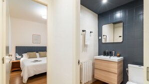 A hotel room with a bed, bedside table, nightstand, and a bathroom with a sink, mirror, and toilet. - Rafael Apartment by Olala Homes (L'Hospitalet de Llobregat)