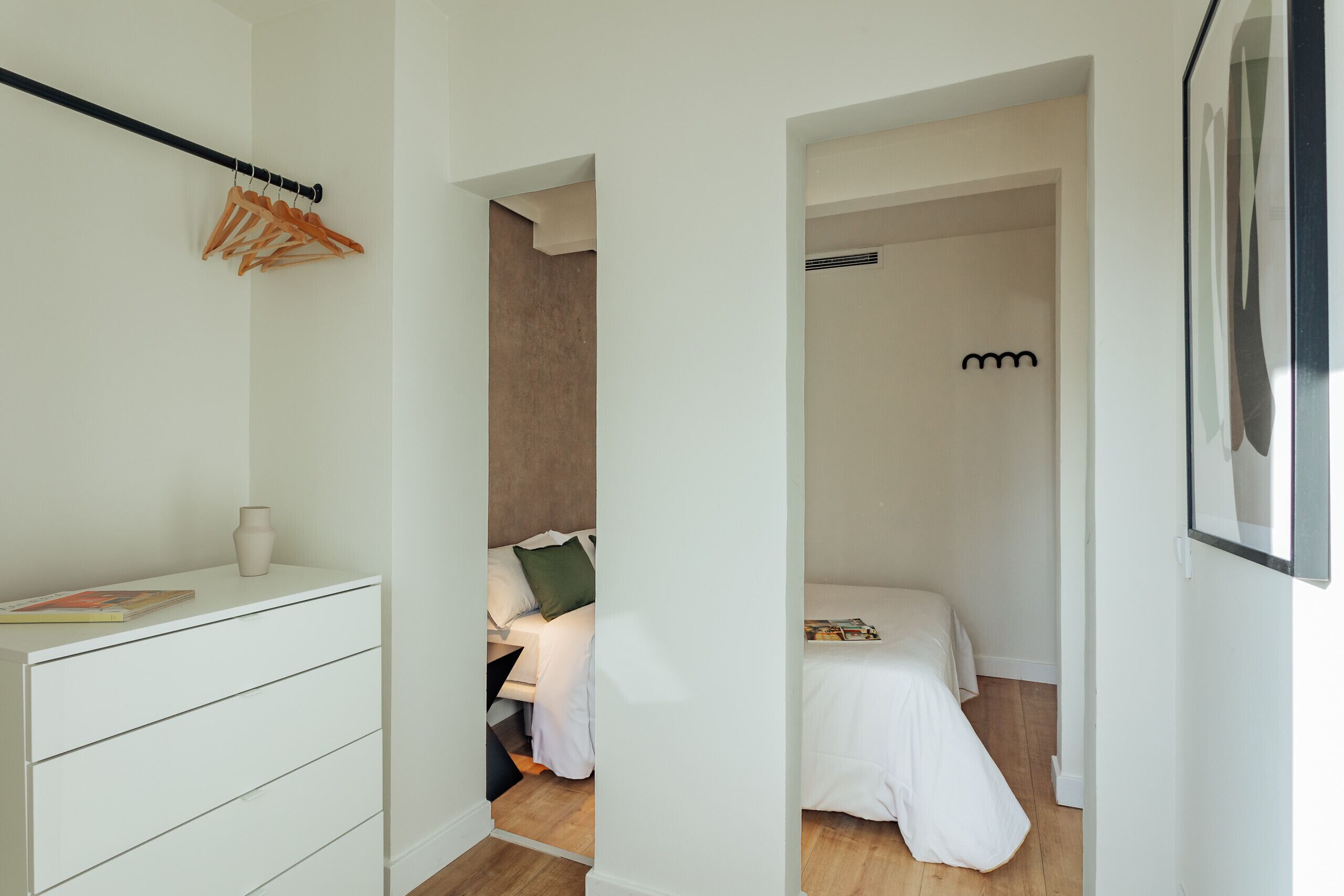 Un dormitorio moderno con un tocador blanco, una cama con ropa de cama blanca y suelo de madera.
