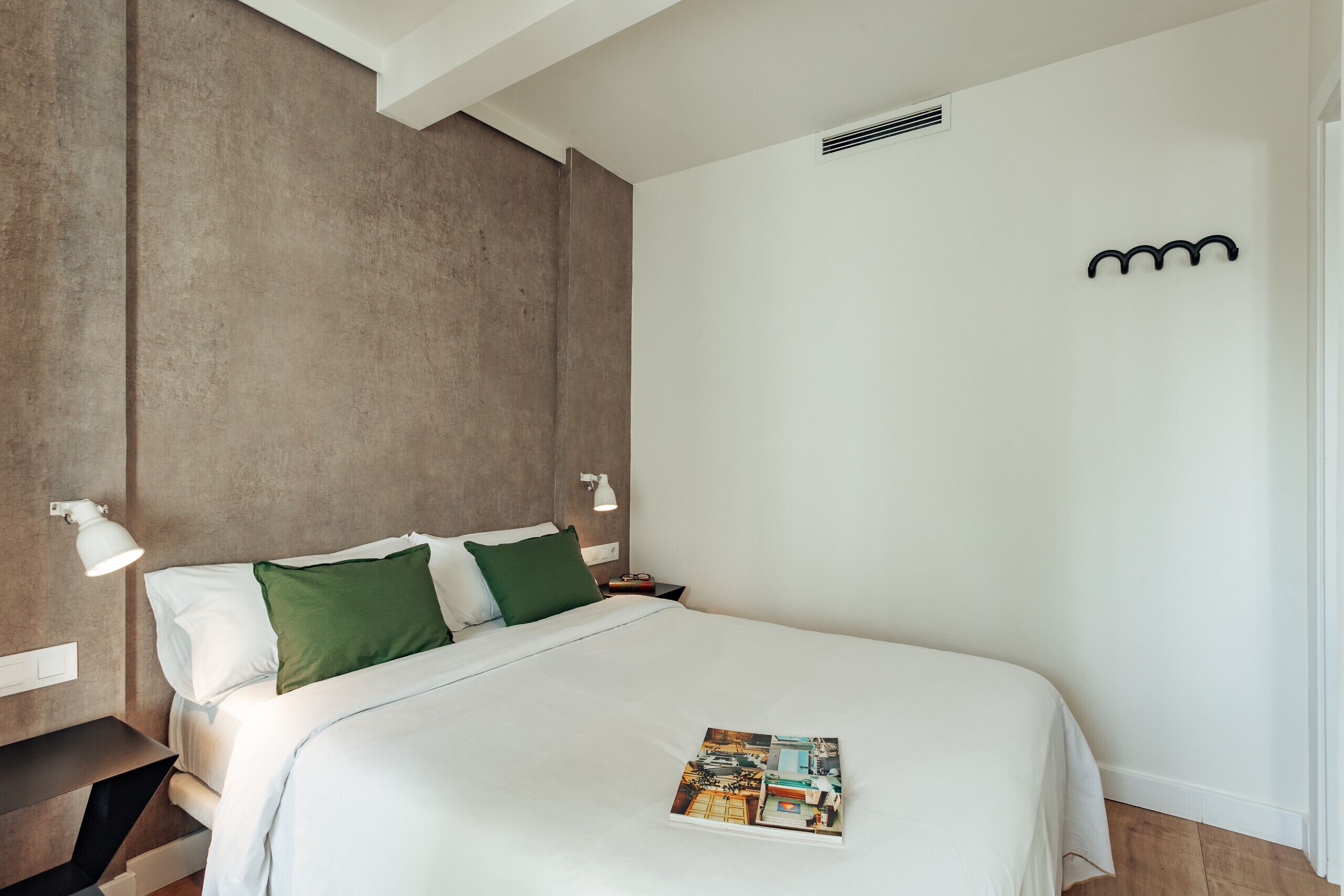 Una habitación de hotel con una cama grande, una mesita de noche, una lámpara y una revista sobre la cama.