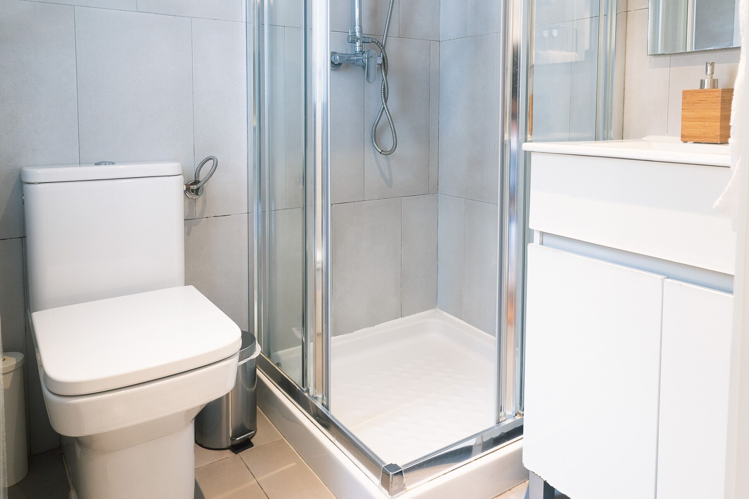 Un baño moderno con inodoro, ducha con mampara de vidrio y lavamanos blanco.
