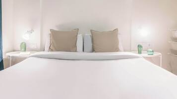 Una habitación de hotel con una cama grande, dos mesitas de noche, una lámpara y un cactus sobre una de ellas.