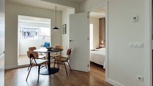 Una habitación moderna con una mesa redonda de comedor, cuatro sillas, una lámpara colgante y una puerta que da a otra habitación.