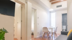 Una sala de estar moderna con un sofá gris, una mesa de comedor con sillas y un televisor montado en la pared.