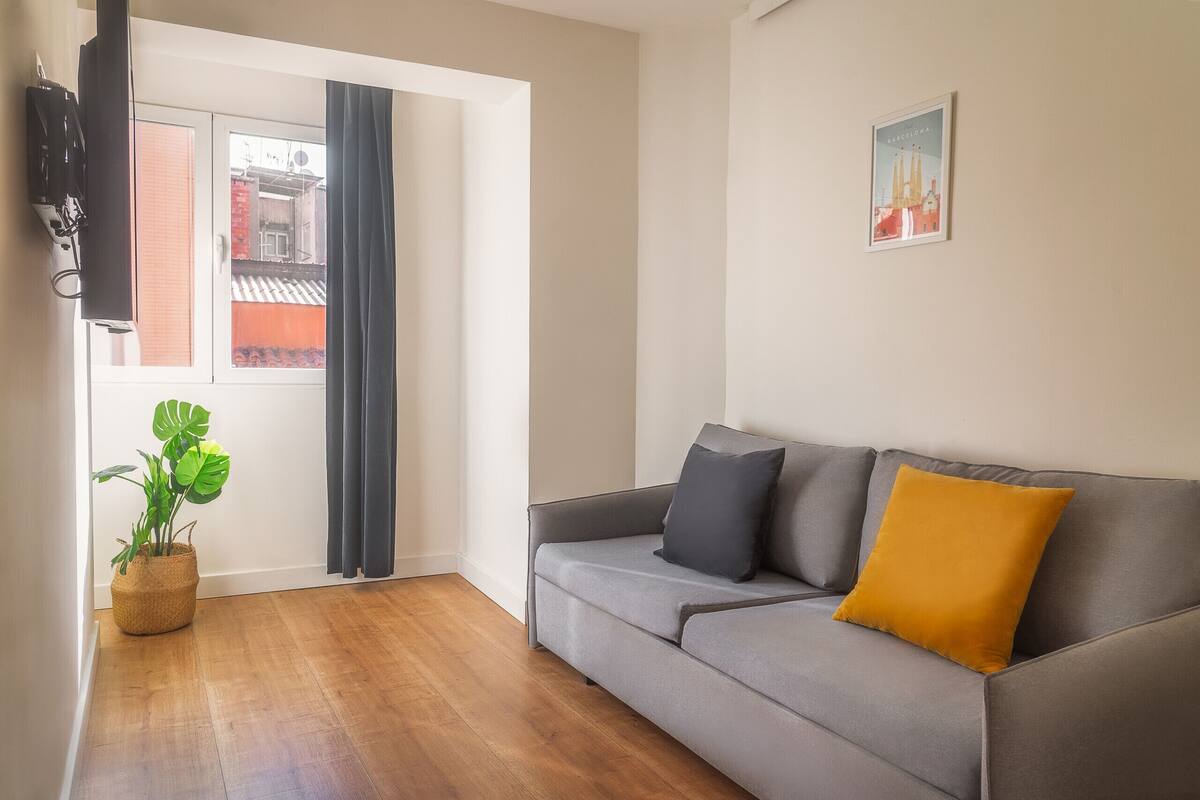 Una sala de estar moderna con un sofá gris, una almohada amarilla y una planta en maceta.