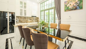 Una cocina moderna con armarios blancos, encimera de mármol y comedor con mesa de vidrio y sillas marrones.
