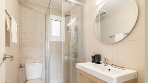 Een moderne badkamer met toilet, douche en wastafel.