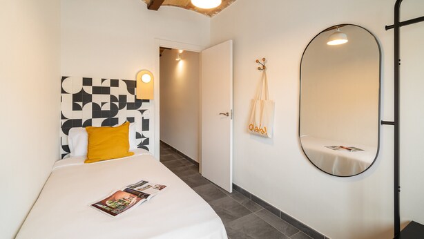 Een slaapkamer met een bed, een ronde spiegel en een deur naar een andere kamer.