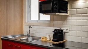 Een keuken met een zwarte magnetron, rode keukenkastjes, een spoelbak en een koffiezetapparaat op een houten plank.