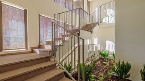A staircase with metal railings leading to an upper level, surrounded by potted plants and a view of the outside.