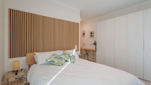 A bedroom with a bed, wooden headboard, bedside table, desk, and wardrobe.
