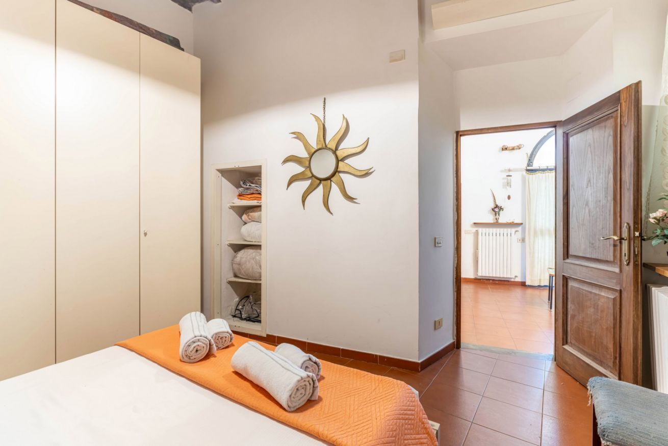 A hotel room with a bed, a sun-shaped wall decoration, a wardrobe, and a view of the outside.