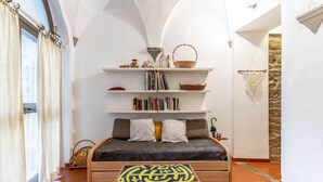 A cozy room with a bed, shelves with books and baskets, a small table with a geometric design, and a stone wall. - GuestHost - Comfortable apartment of approximately 50 square meters, able to accommodate up to 4 people, located on the ground floor of an ancient building, but in good condition. The apartment is located in the Porta Romana-Boboli district (Traffic-Rest (Firenze)