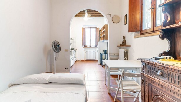A narrow room with a bed, a fan, a table, and a wooden cabinet. - GuestHost - Comfortable apartment of approximately 50 square meters, able to accommodate up to 4 people, located on the ground floor of an ancient building, but in good condition. The apartment is located in the Porta Romana-Boboli district (Traffic-Rest (Firenze)