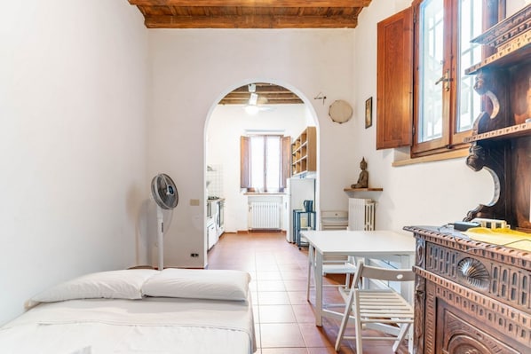 A narrow room with a bed, a fan, a table, and a wooden cabinet.