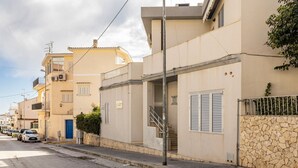 A residential street with beige buildings, a stone wall, and a blue door. - GuestHost - Cozy 25 sqm studio apartment, perfect for 2 people, located on the first floor of a renovated building without a lift. The property is located in the center of Marina di Ragusa (20 km from Ragusa), one of the most renowned seaside areas in Si (Marina di Ragusa)