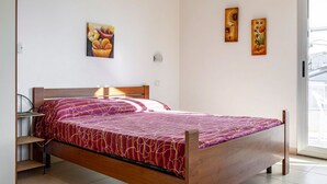 A bed with a patterned bedspread, a bedside table, and a wall-mounted lamp. - GuestHost - Cozy 25 sqm studio apartment, perfect for 2 people, located on the first floor of a renovated building without a lift. The property is located in the center of Marina di Ragusa (20 km from Ragusa), one of the most renowned seaside areas in Si (Marina di Ragusa)