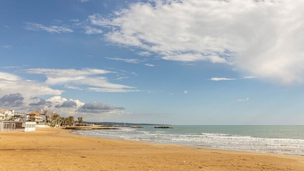 Une plage bordée de bâtiments, un ciel dégagé et une mer calme.