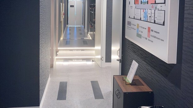 A hotel corridor with a reception desk, a map of the hotel layout, and a sign indicating the direction to the lobby. - Capsule Hotel Nagasaki (Nagasaki)