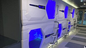 A row of white, futuristic-looking pods with blue lighting accents and metallic handles. - Capsule Hotel Nagasaki (Nagasaki)