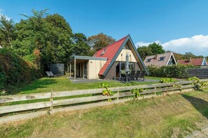 Un pequeño edificio de forma triangular con techo rojo, rodeado de una cerca de madera y follaje.