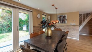 A dining area with a large table, chairs, and a vase of flowers. There is a clock on the wall and a staircase in the background. - Holiday Home Groote Keeten near Beaches (Groote Keeten)