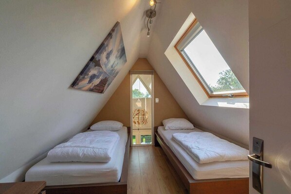 A small, well-lit room with two single beds, a skylight, and a painting on the wall.