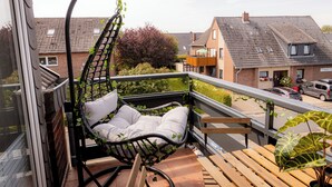 A balcony with a hanging chair, wooden bench, and potted plant. - "Küstenruhe" - your retreat at the Deichkieker guesthouse - pets allowed (Wangerland)