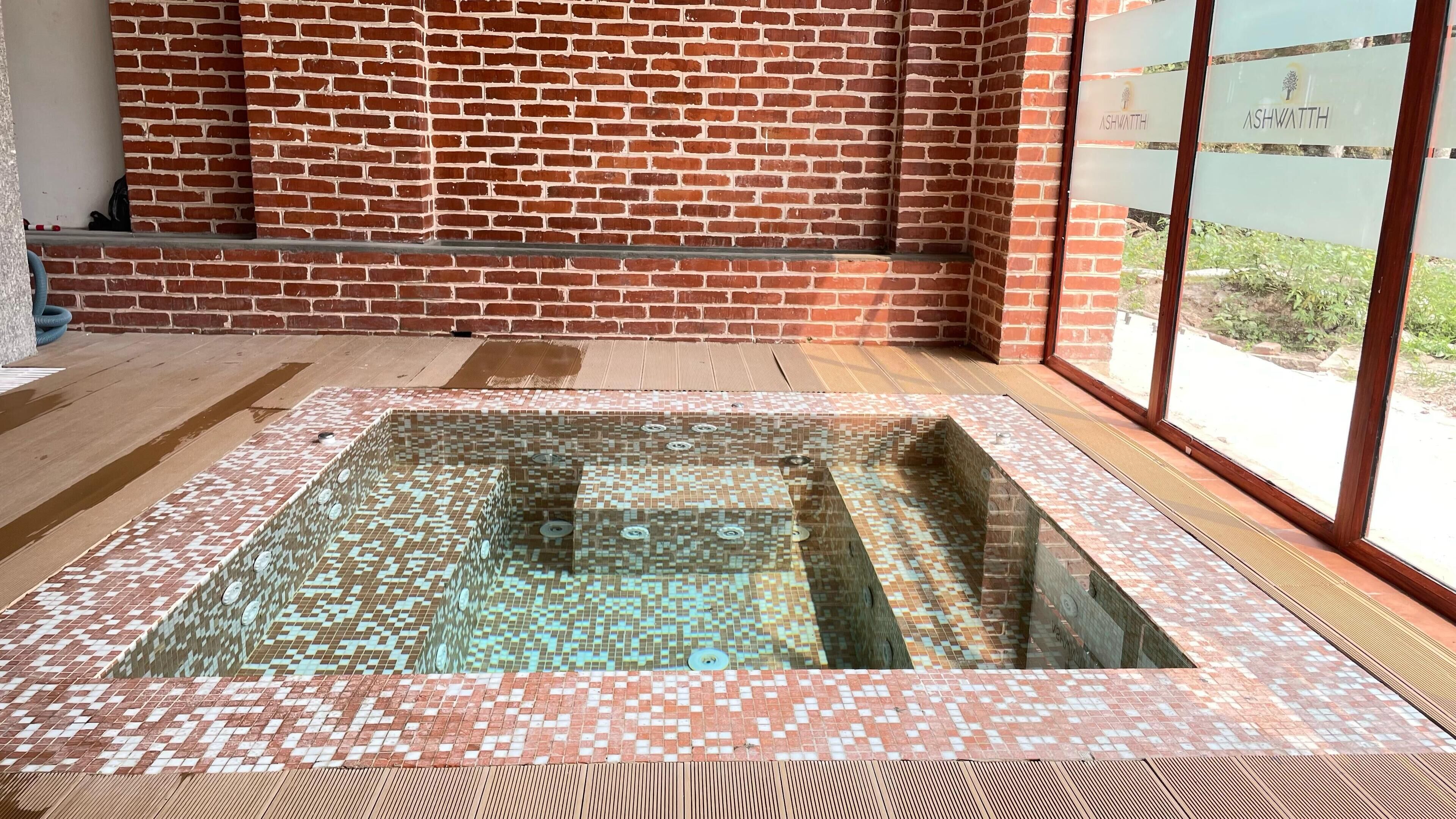 A spa area with a tiled hot tub, wooden flooring, and a brick wall.