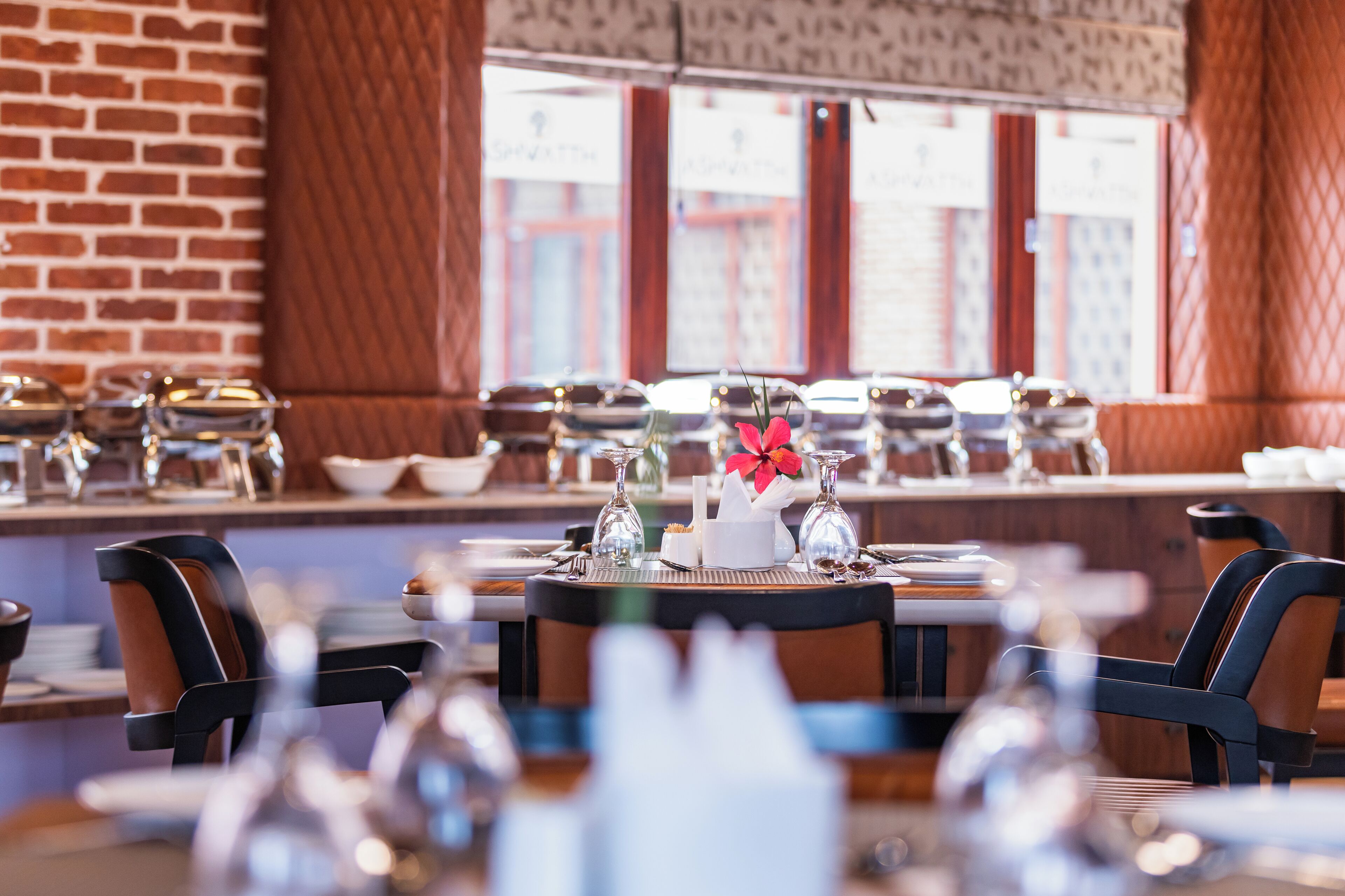 A restaurant with a brick wall, large windows, and tables set with glassware and a centerpiece.