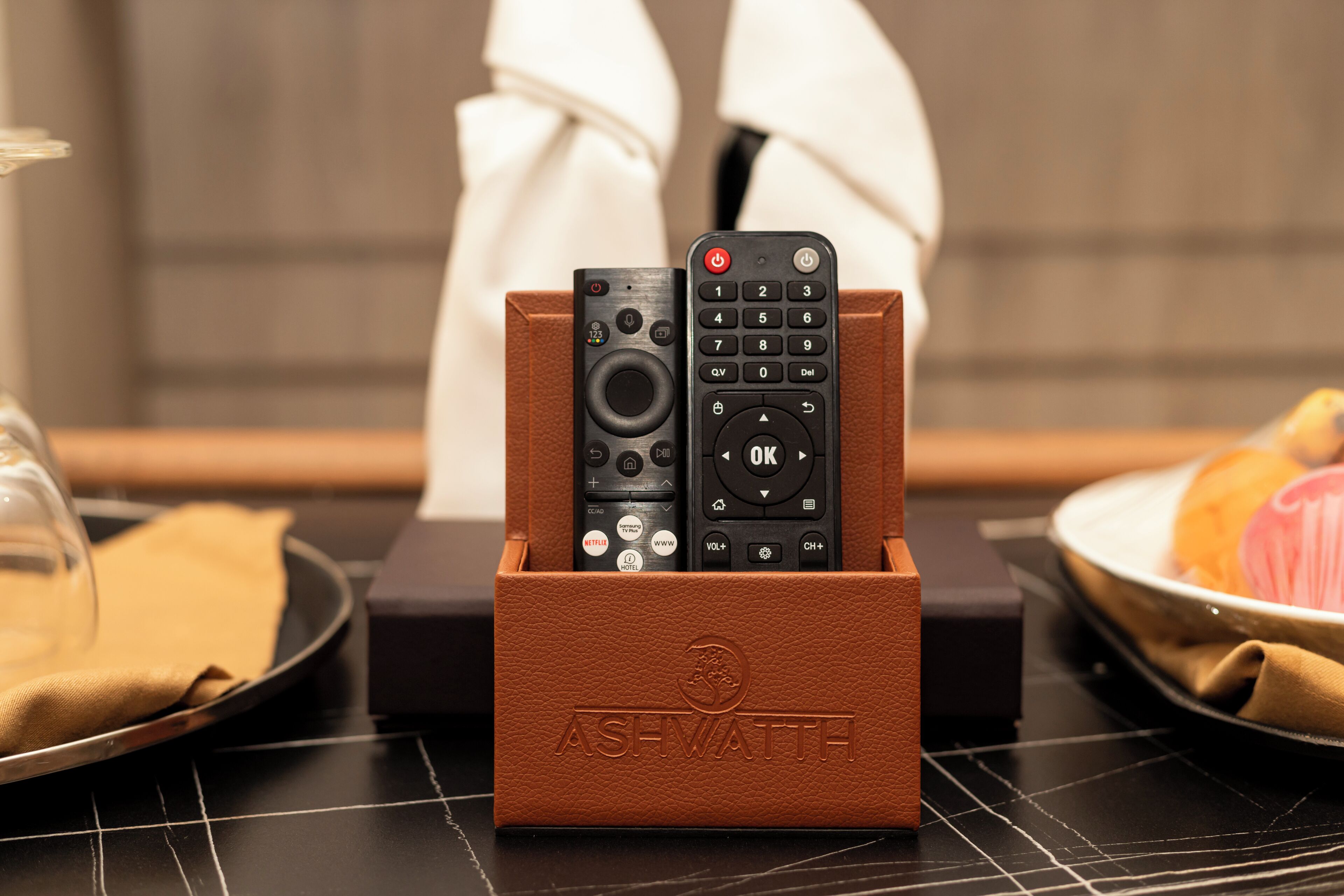 A remote control holder with three remote controls, a smartphone, and a cup of coffee on a table.