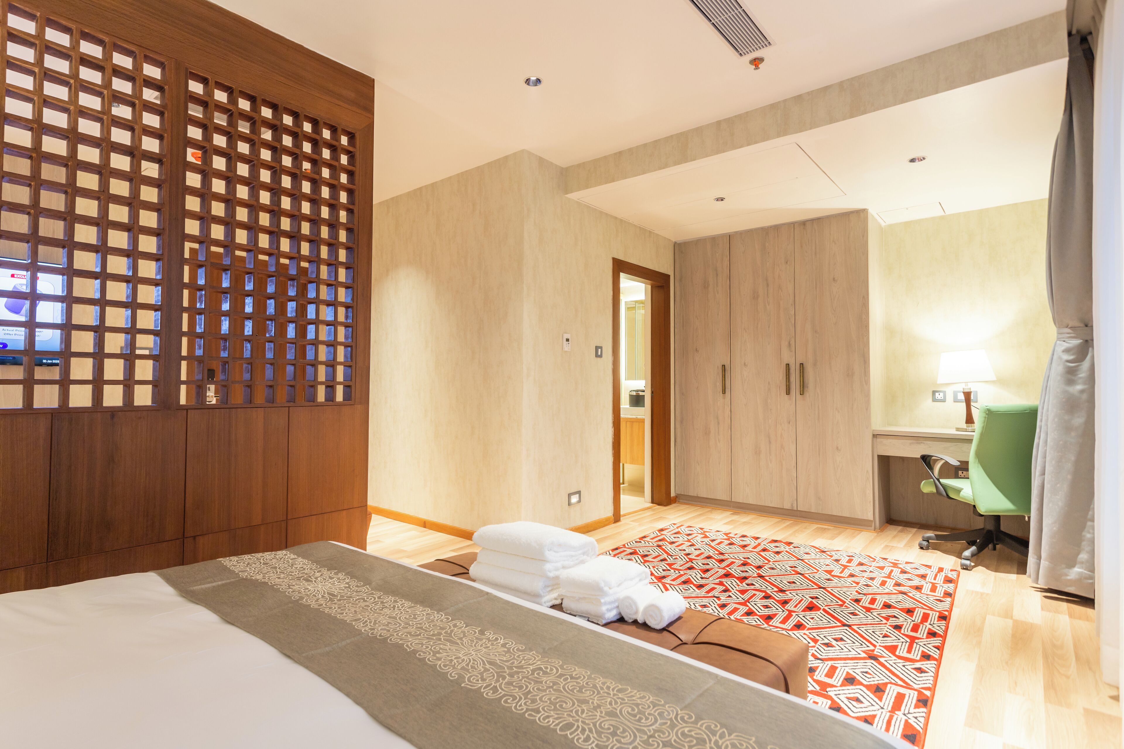 A hotel room with a bed, a desk, a chair, and a bathroom visible through an open door.