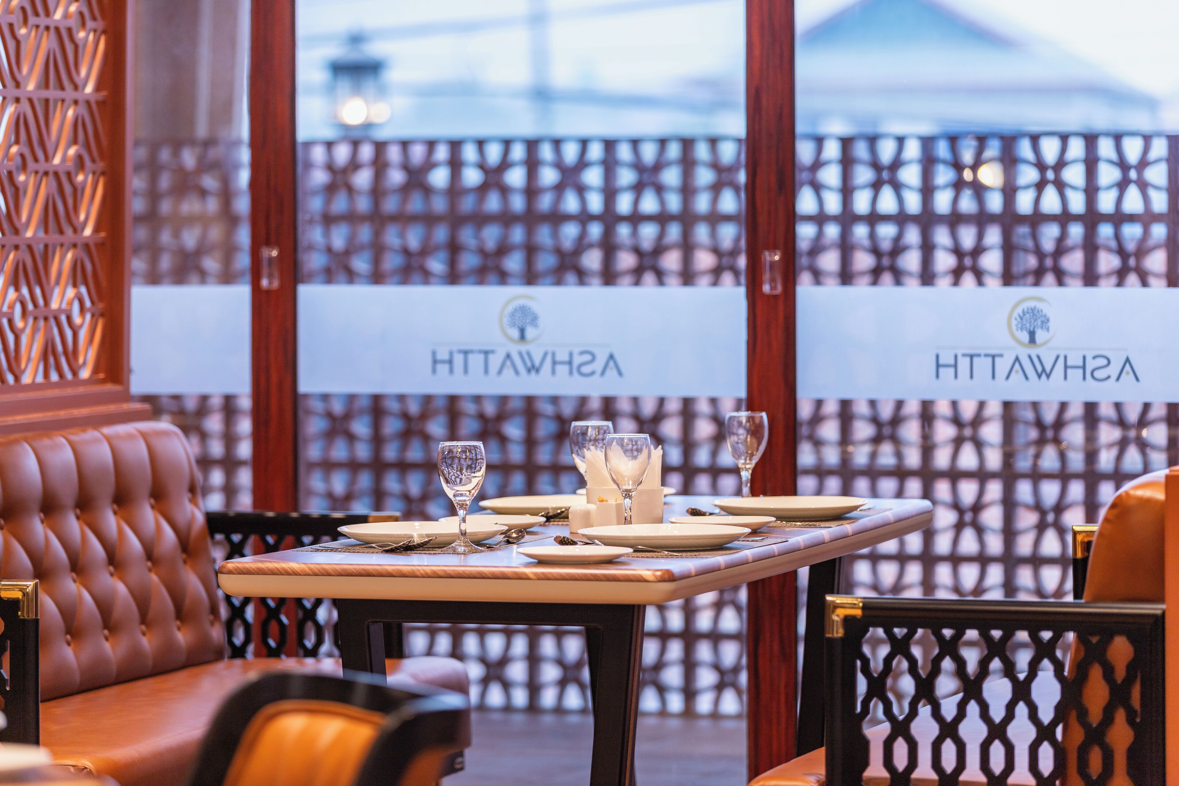 A dining table set with plates, glasses, and cutlery, with a sign reading "ASHAWHTT" in the background.